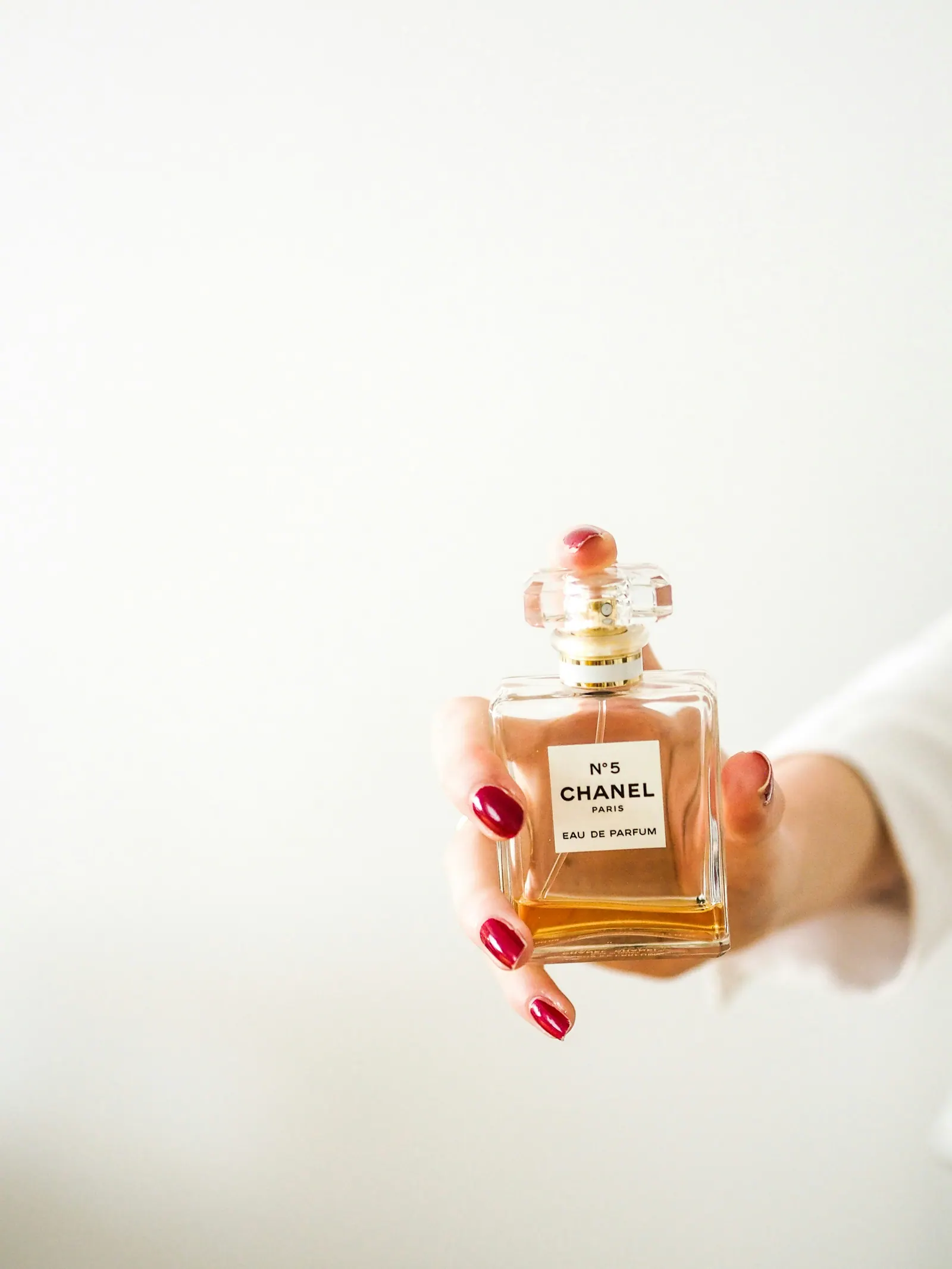 A hand holding a small amber flacon against a white wall