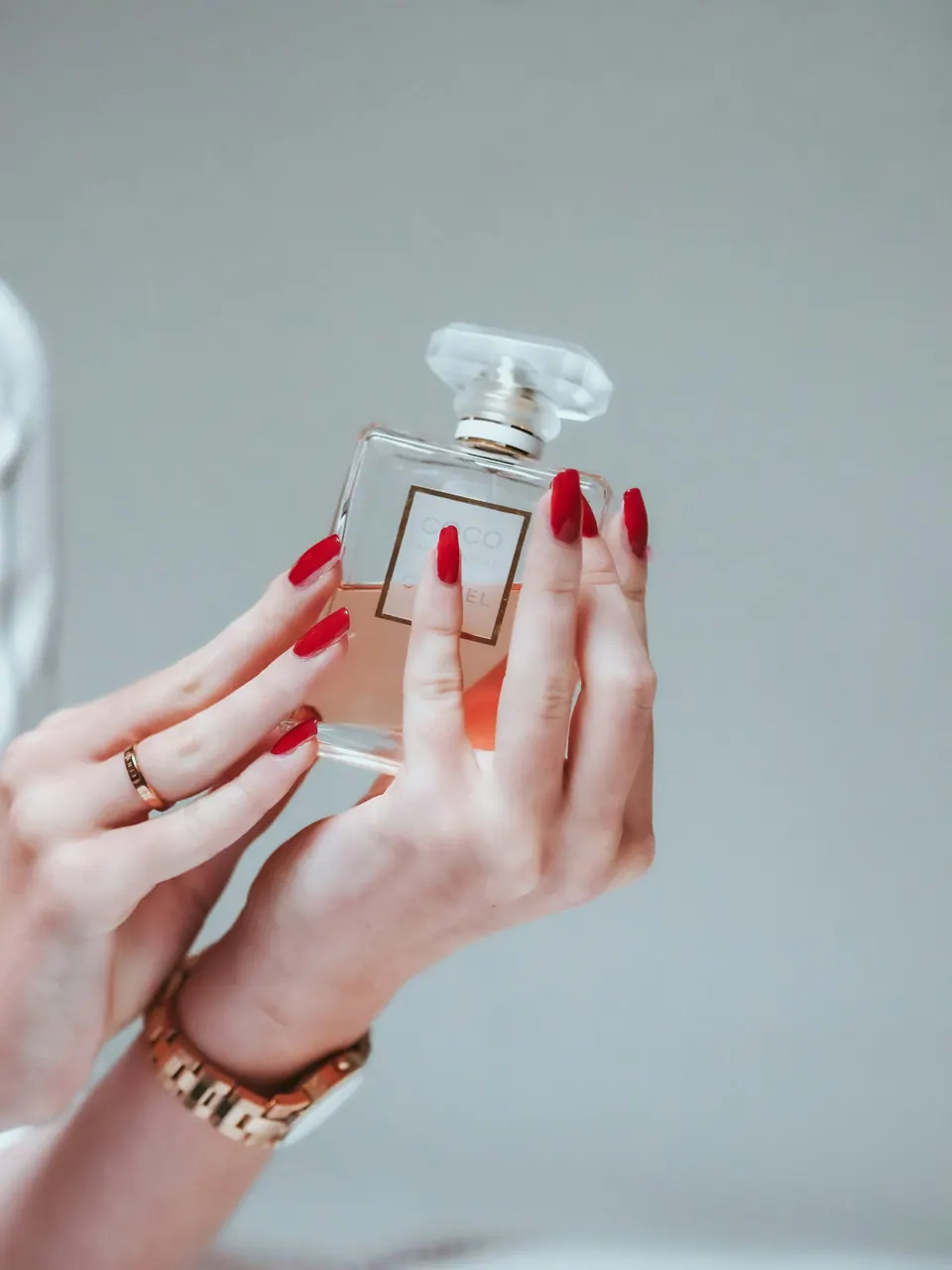 Two hands holding a flacon against a soft grey wall