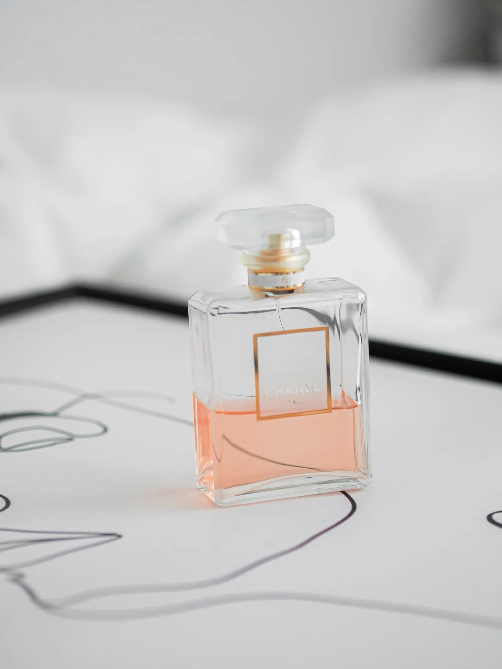 Glass flacon with pale peach fragrance standing on white linen over a line drawing