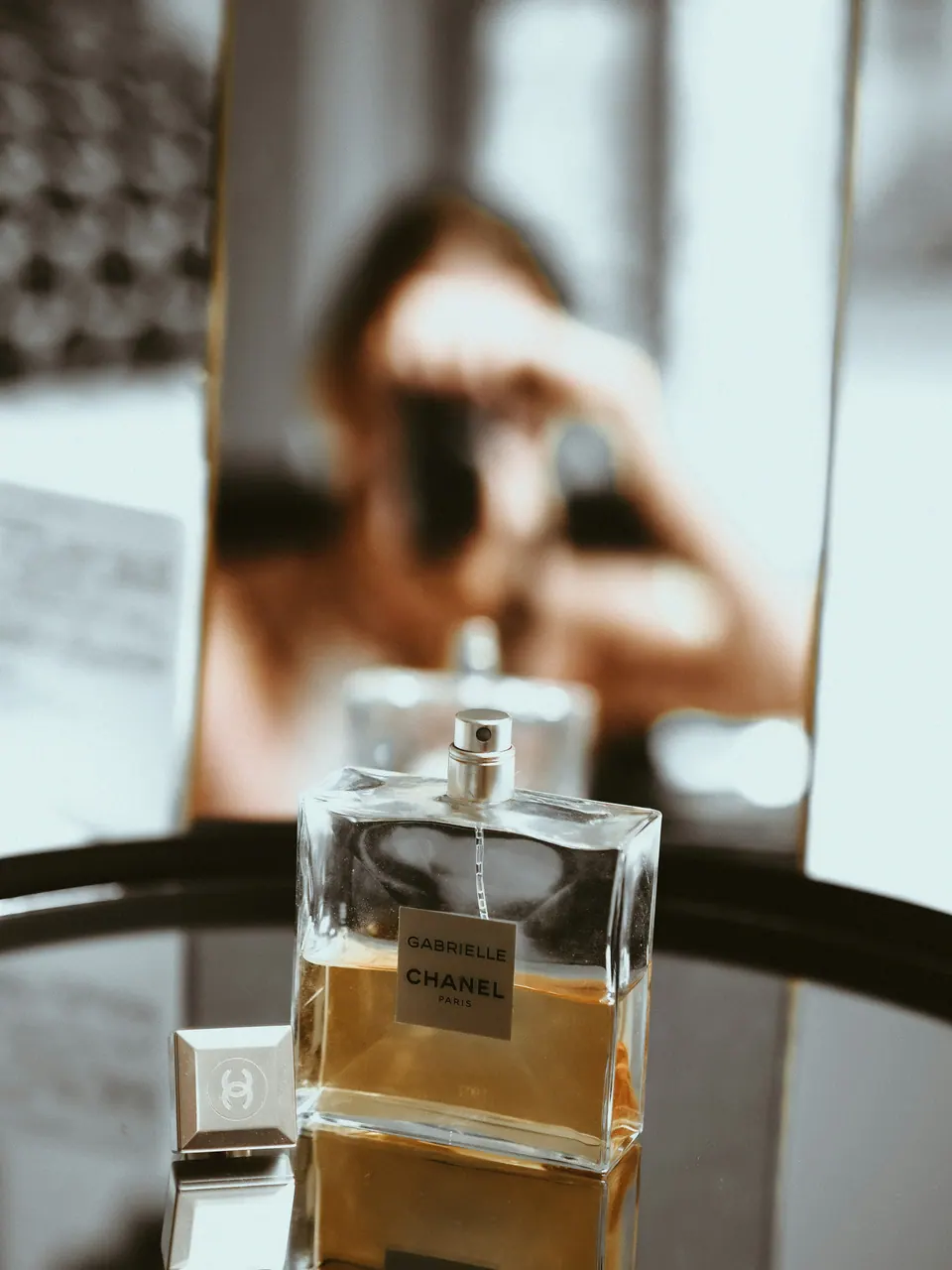 Flacon on a mirrored table with a blurred photographer reflected