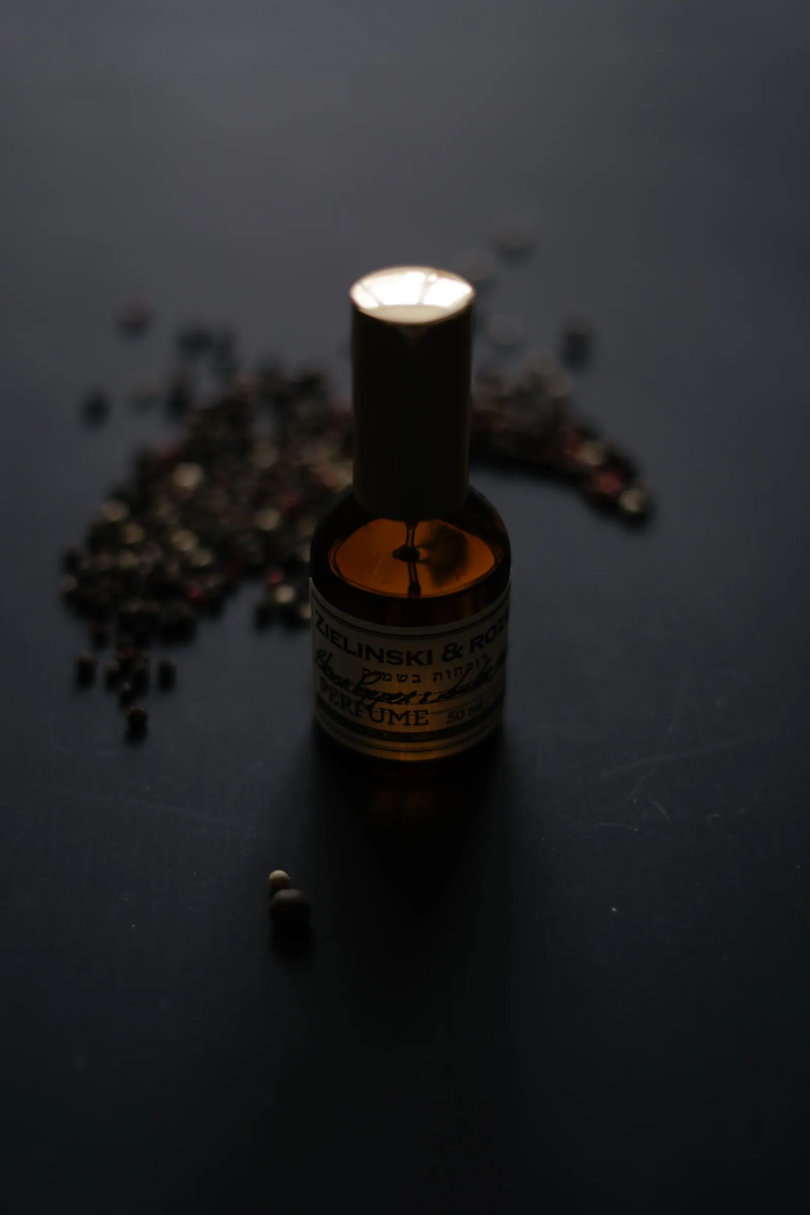 Dark amber flacon surrounded by scattered peppercorns on black