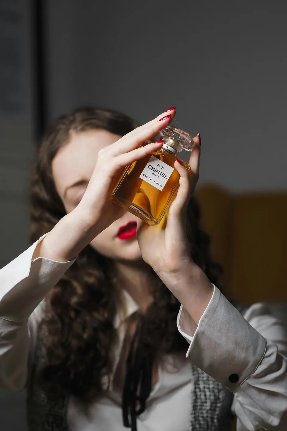 A woman holding an amber flacon in front of her face, dark interior